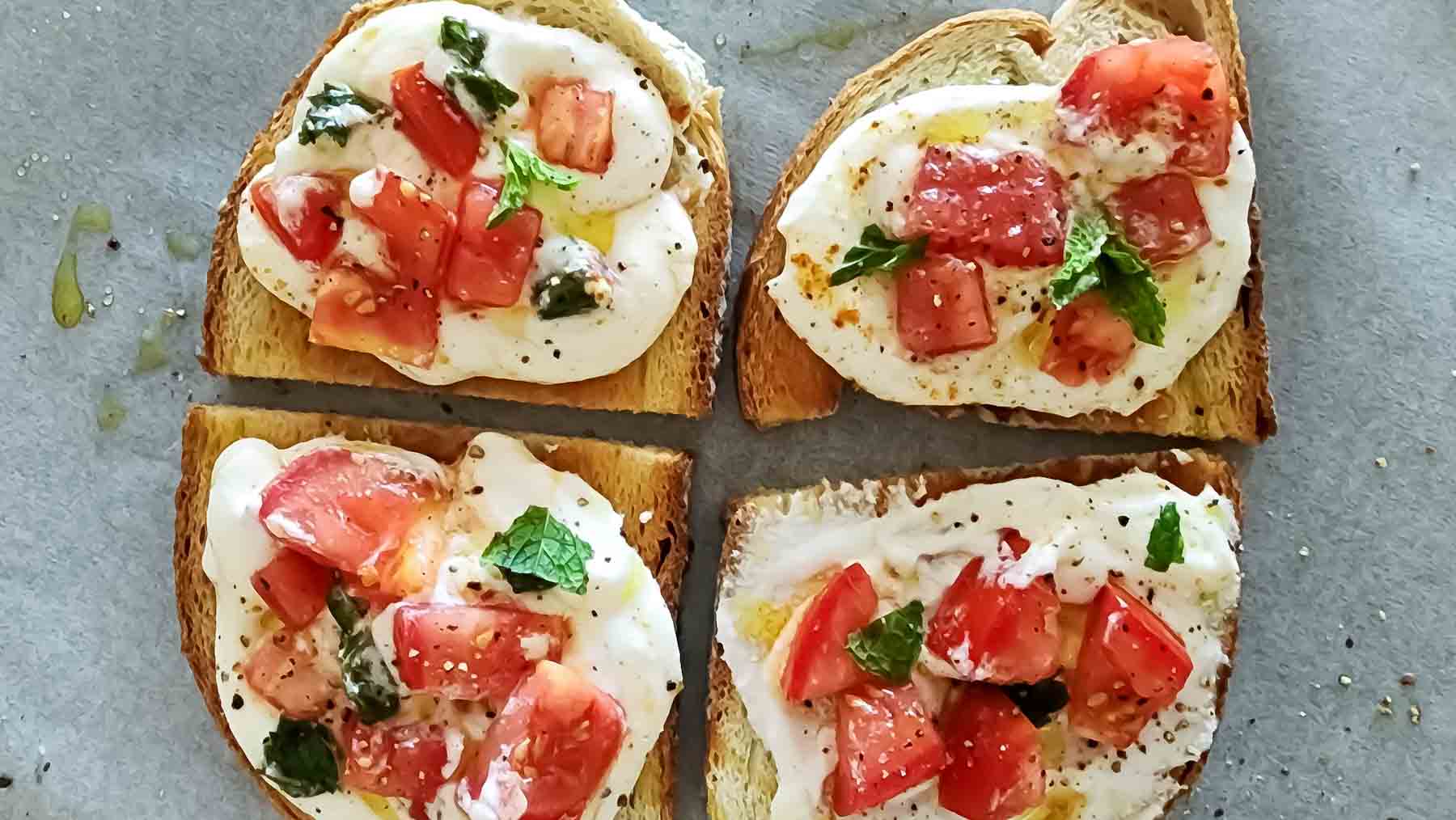 A tray full of crostini with cottage cheese and tomatoes.