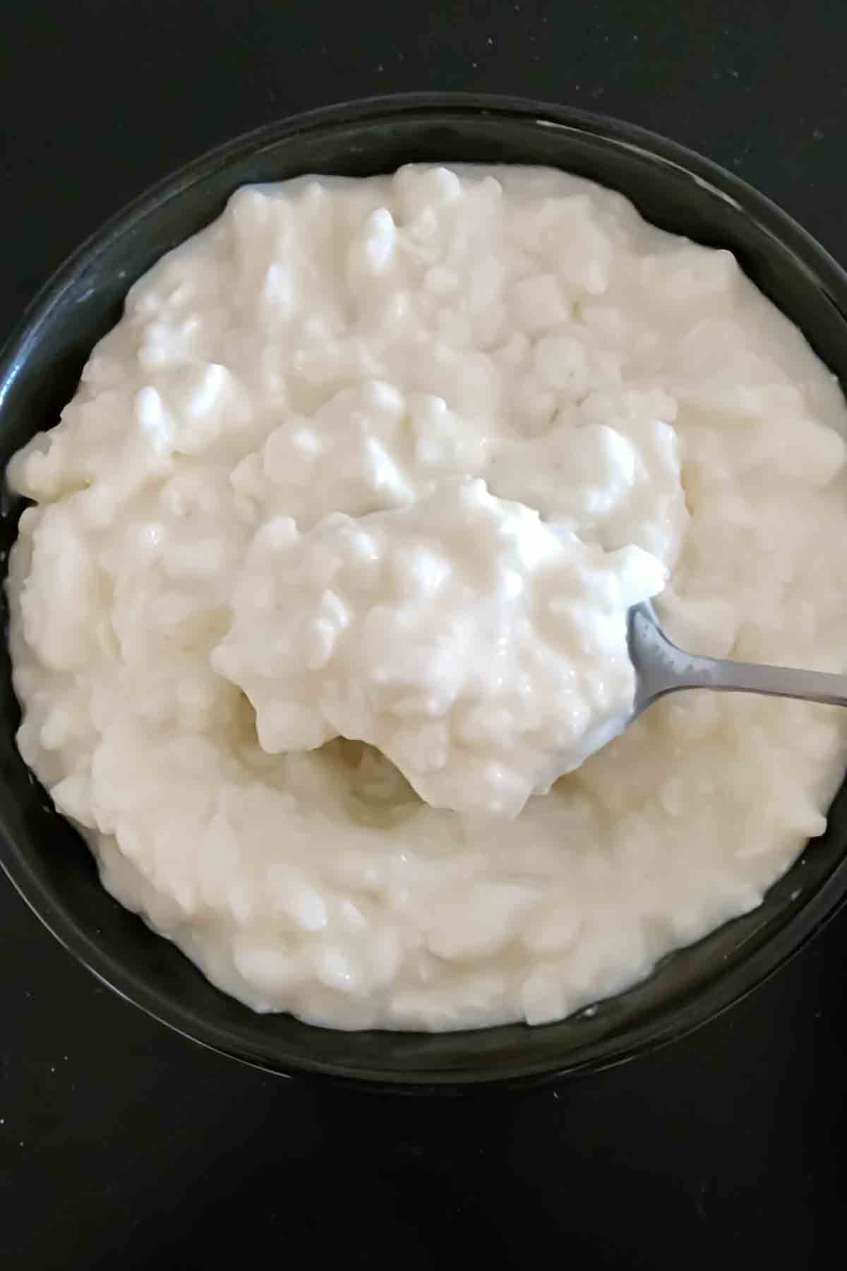 A bowl of fresh cottage cheese with a spoon.