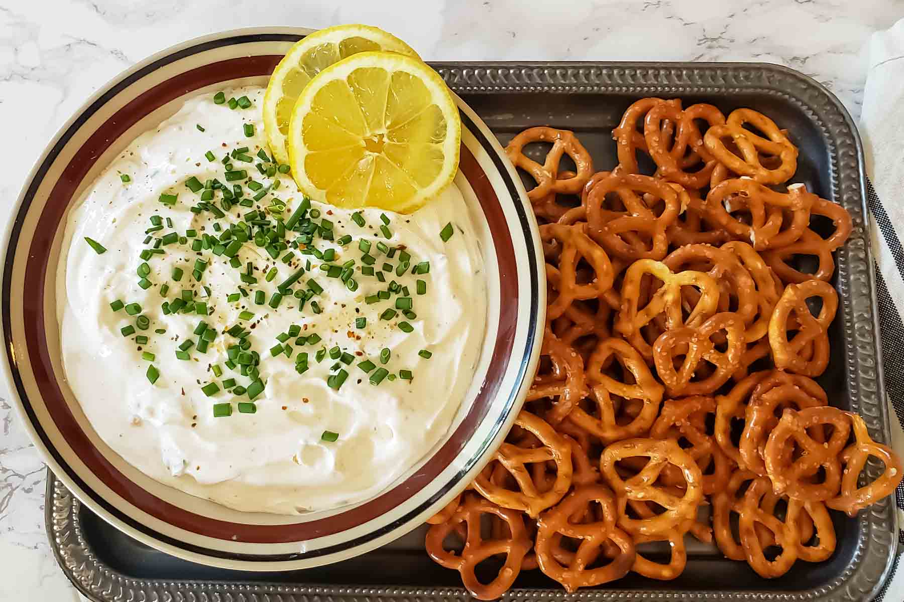 Prepared sour cream and chive dip served with garnishes and pretzel twists.