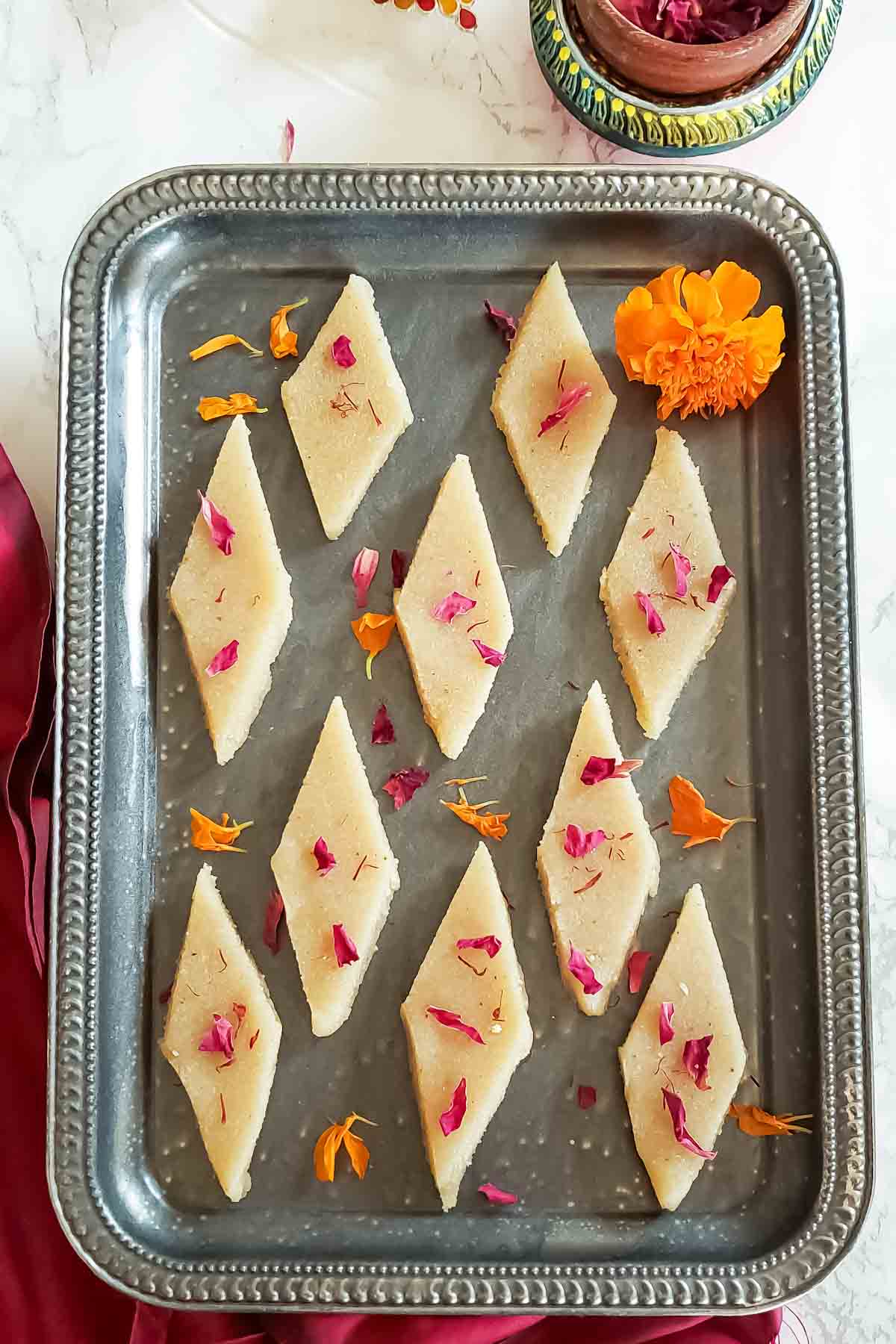 A try full of badam burfi garnishes with saffron and rose petals.