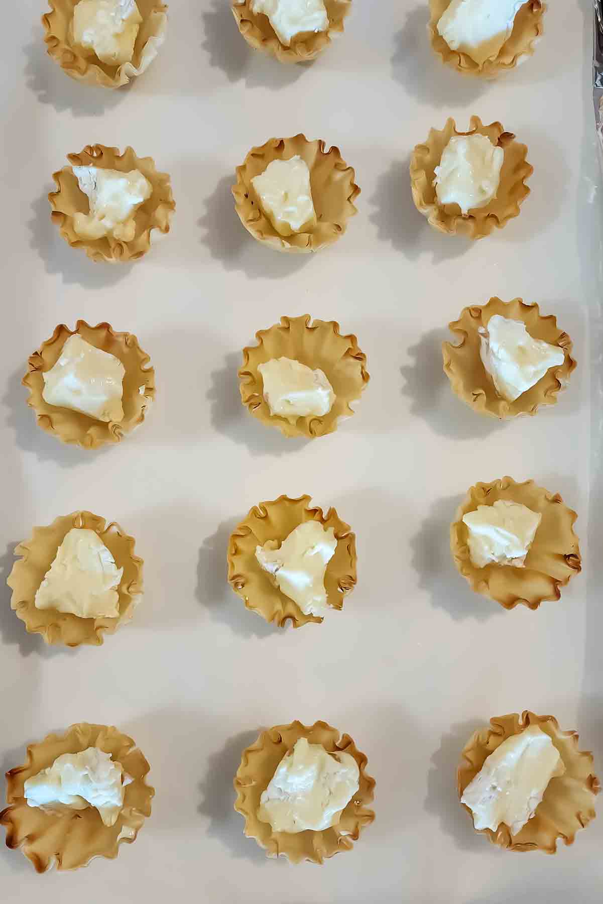 Step one of arranging the phyllo cups and adding pieces of brie cheese.