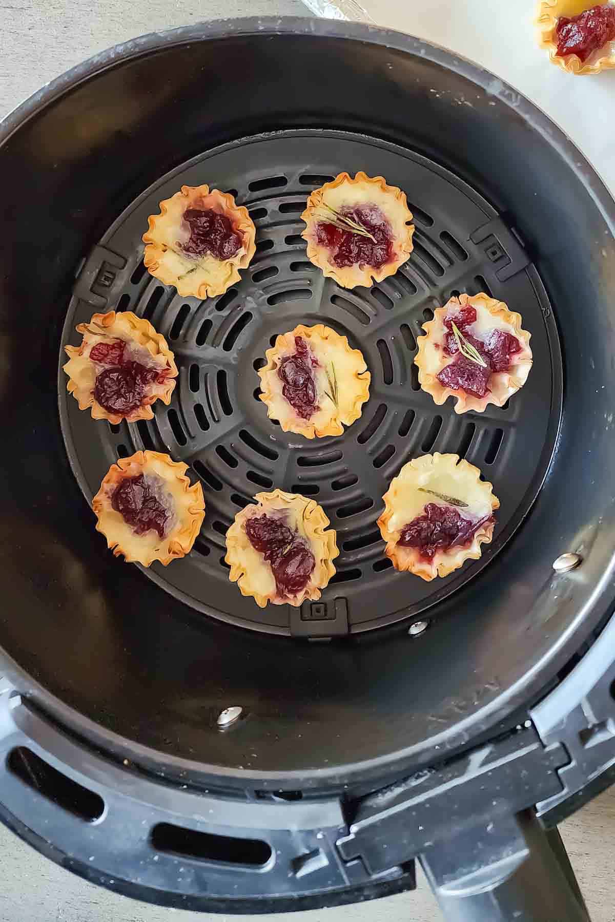Phyllo cups filled with brie cheese and cranberry sauce arranged in the air fryer basket.