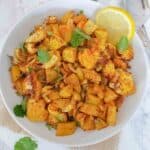 Aloo gobi which is dry Indian curry made with potato and cauliflower served with garnishes.
