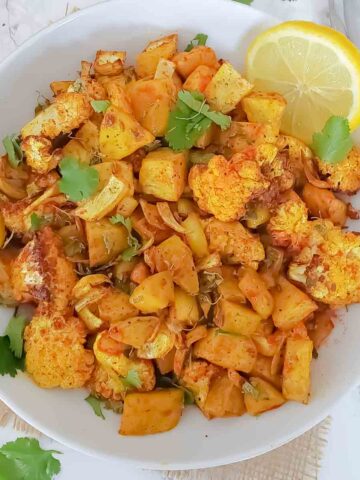 Aloo gobi which is dry Indian curry made with potato and cauliflower served with garnishes.