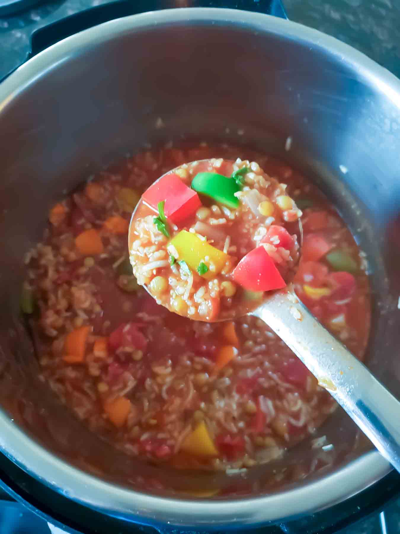 A ladle full of cooked bell pepper soup with rice and lentil which makes it complete one pot meal.