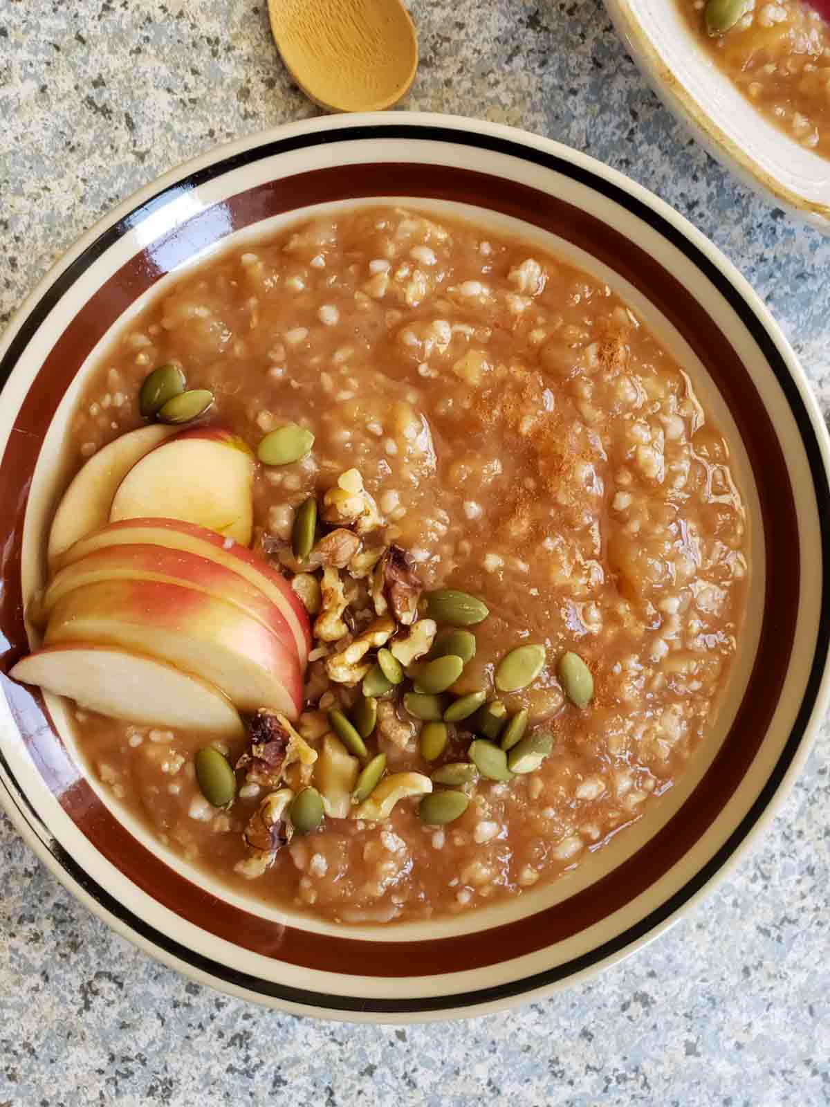 Cozy comforting bowl of apple pie oatmeal served for breakfast with toppings.