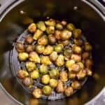 Brussels sprouts tossed with maple balsamic sauce in air fryer basket.