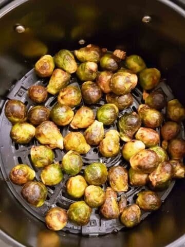 Brussels sprouts tossed with maple balsamic sauce in air fryer basket.