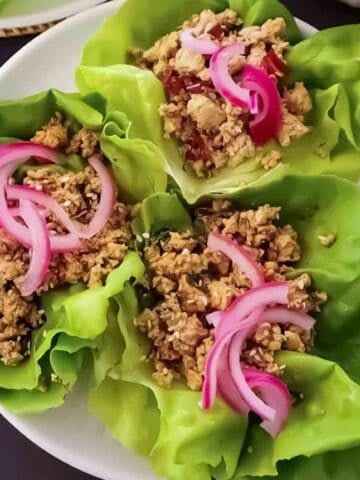 Ground tofu lettuce wraps with spicy ginger miso sauce, pickled red onions, and toasted sesame seeds in butter lettuce cups.