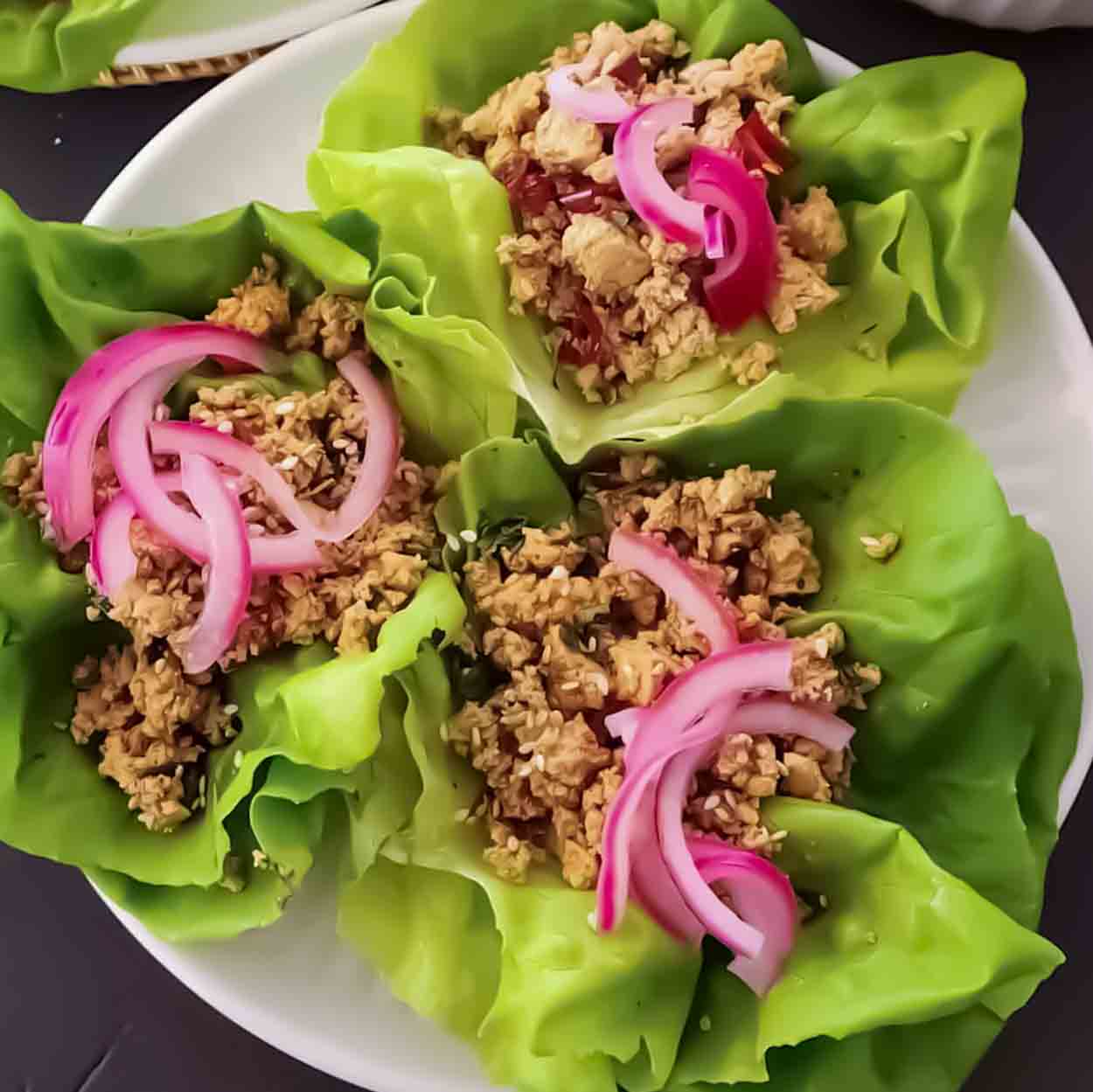 Ground tofu lettuce wraps with spicy ginger miso sauce, pickled red onions, and toasted sesame seeds in butter lettuce cups.